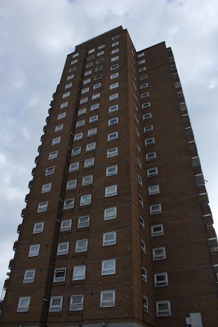 A tall multi-storey residential building constructed with brown brick, featuring numerous white-framed windows arranged in a grid pattern across its vertical façade. The building extends high into the